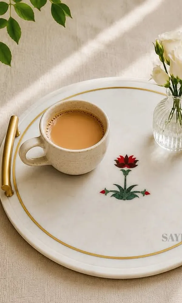 White marble tray with a hand-inlaid red flower and brass handles, holding a cup of chai